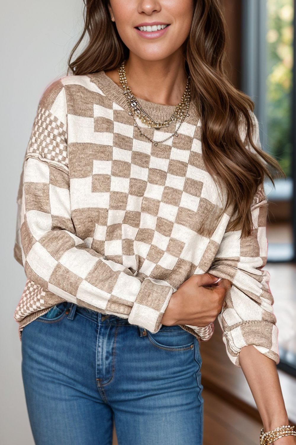 Checkered round neck long sleeve sweater in beige and white pattern.